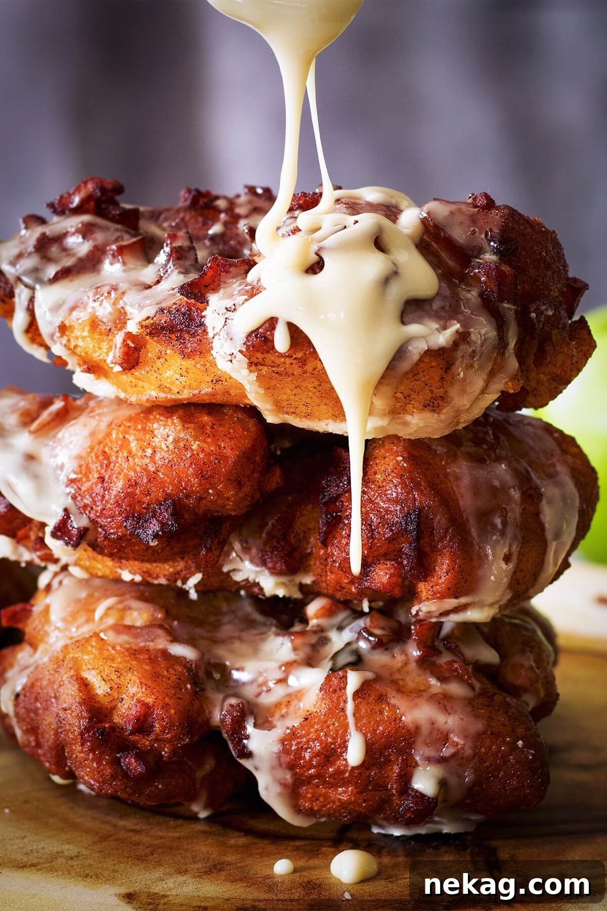 A stack of perfectly glazed apple fritters, with a generous pour of maple glaze cascading over them.