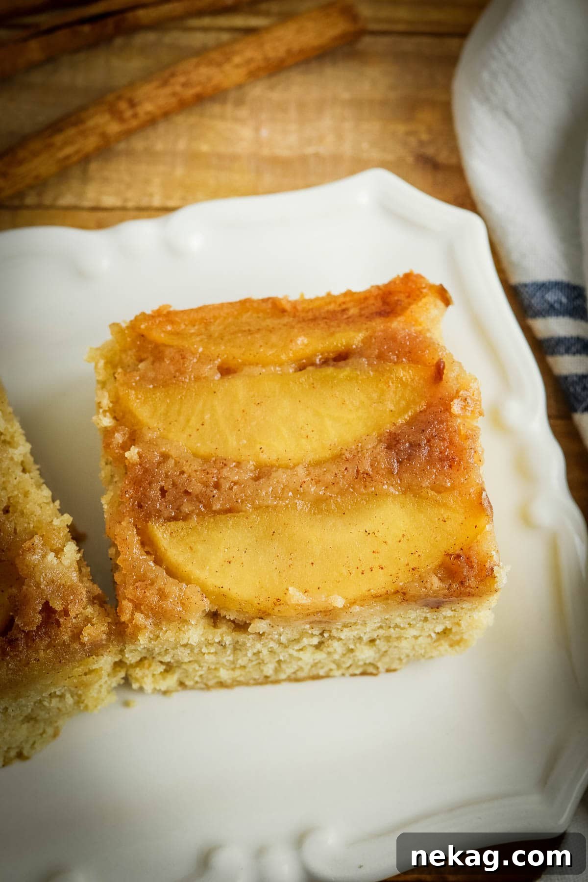 A generous slice of apple upside-down cake presented on a elegant white cake plate, showing off its caramelized apple topping.