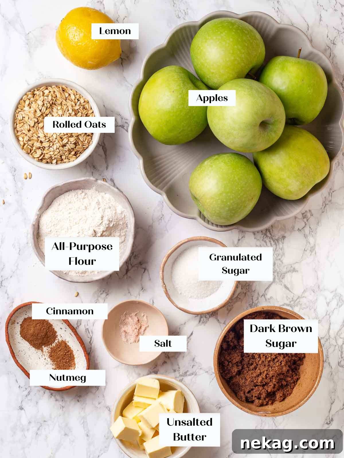 Effortless Golden Apple Crisp 4 Ingredients for apple crisp laid out on a marble surface, including apples, cinnamon, lemon, and oats.