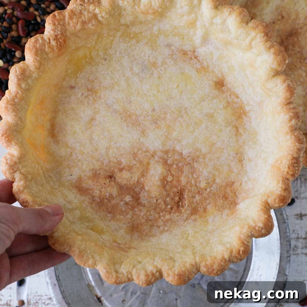 Mastering Blind Baking for a Perfect Pie Crust 13 A perfectly partially blind baked pie crust held gently in a hand, showcasing its golden edge and smooth interior.