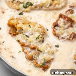 Pork chop in a pan with creamy mushroom sauce and fresh thyme garnish.