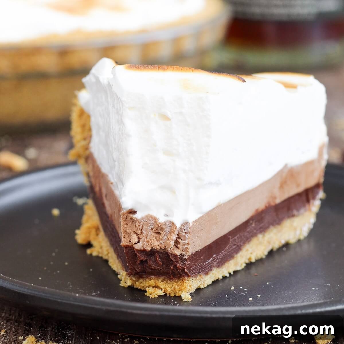 Heavenly Marshmallow Frosting 10 Close-up of a decadent whiskey s'mores pie with toasted marshmallow topping on a black plate.