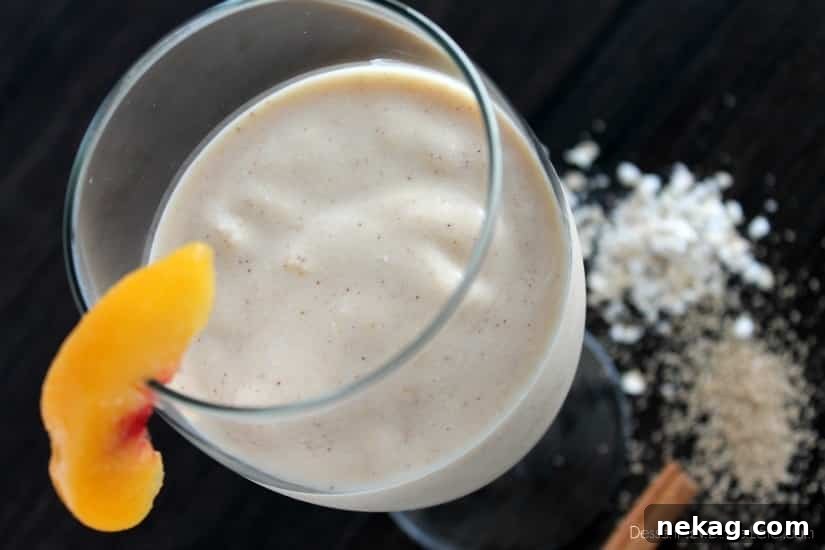 A tall glass of Peach Cobbler Smoothie garnished with a fresh peach slice