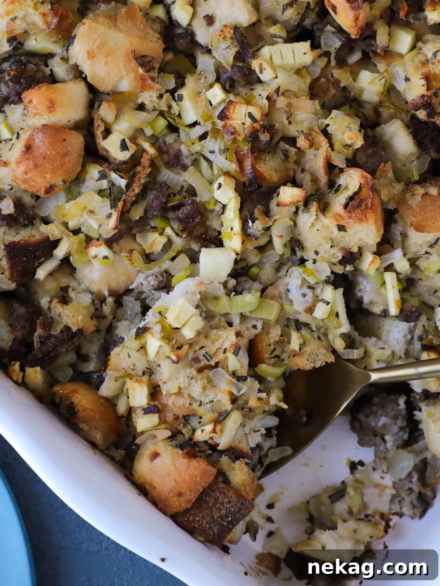 Apple Sage Sausage Stuffing in a white baking dish with a spoon, highlighting the golden-brown crust and moist interior.