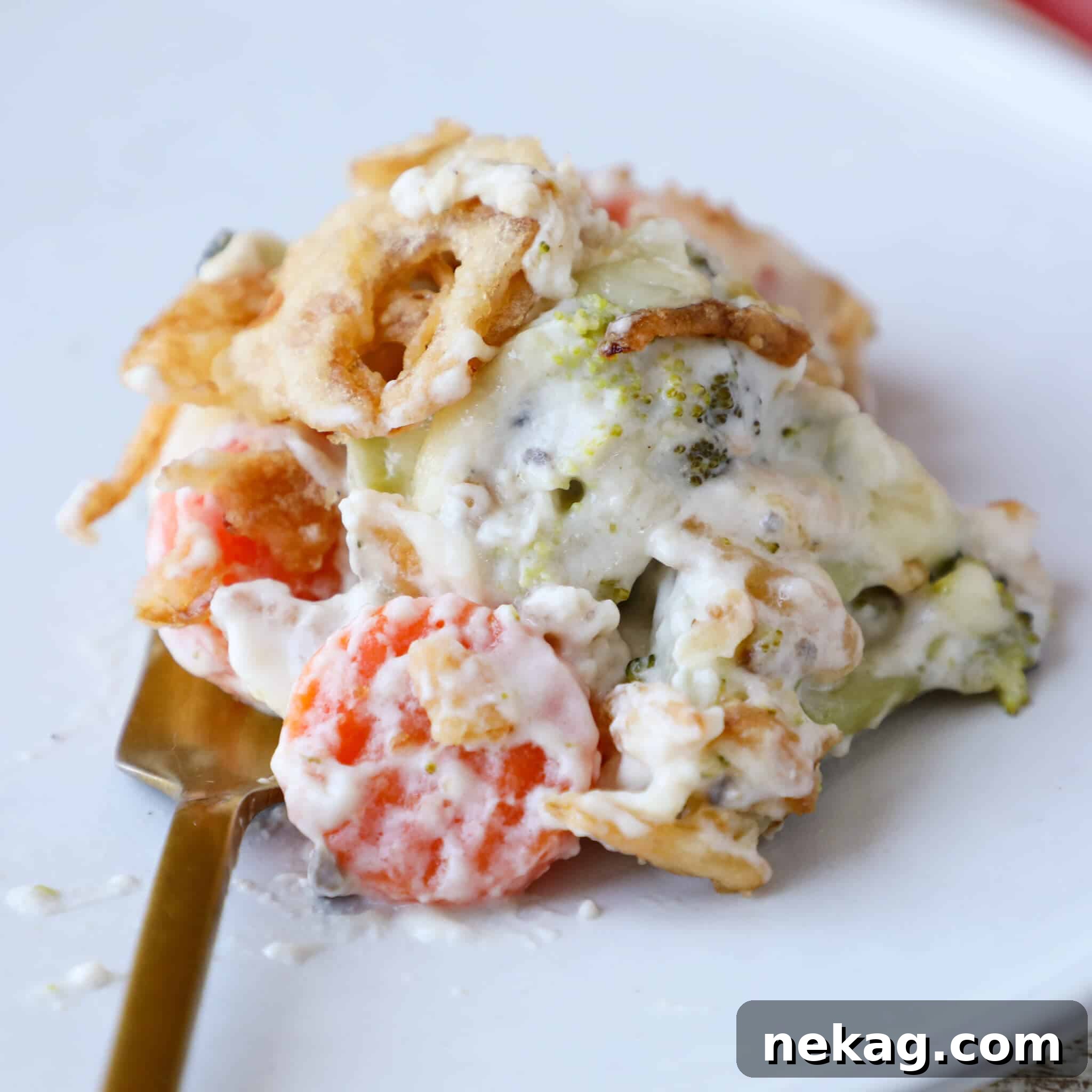 A serving of vegetable casserole on a white plate with a gold fork.