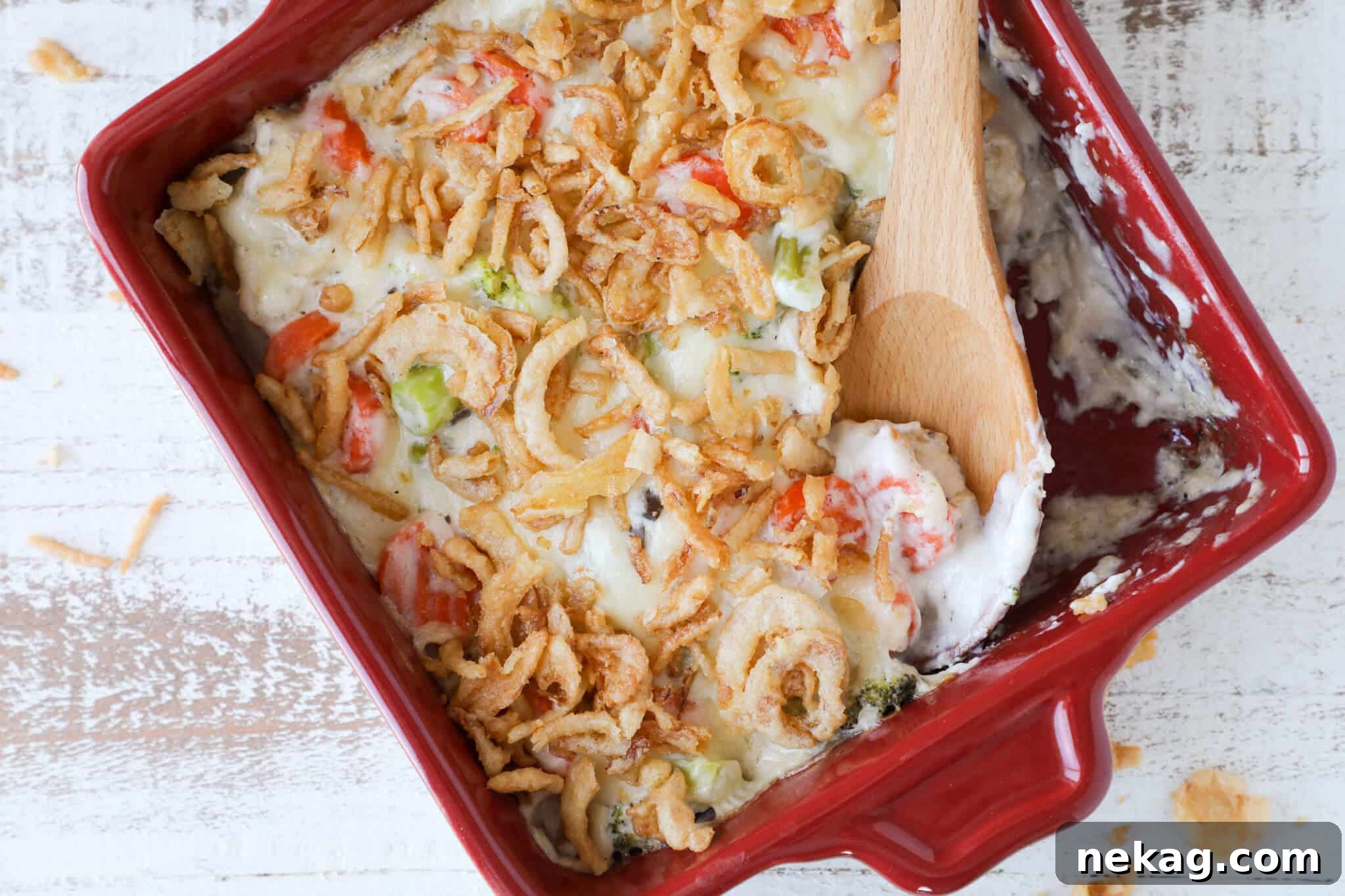 Baked vegetable casserole in a red dish with crunchy onions on top.