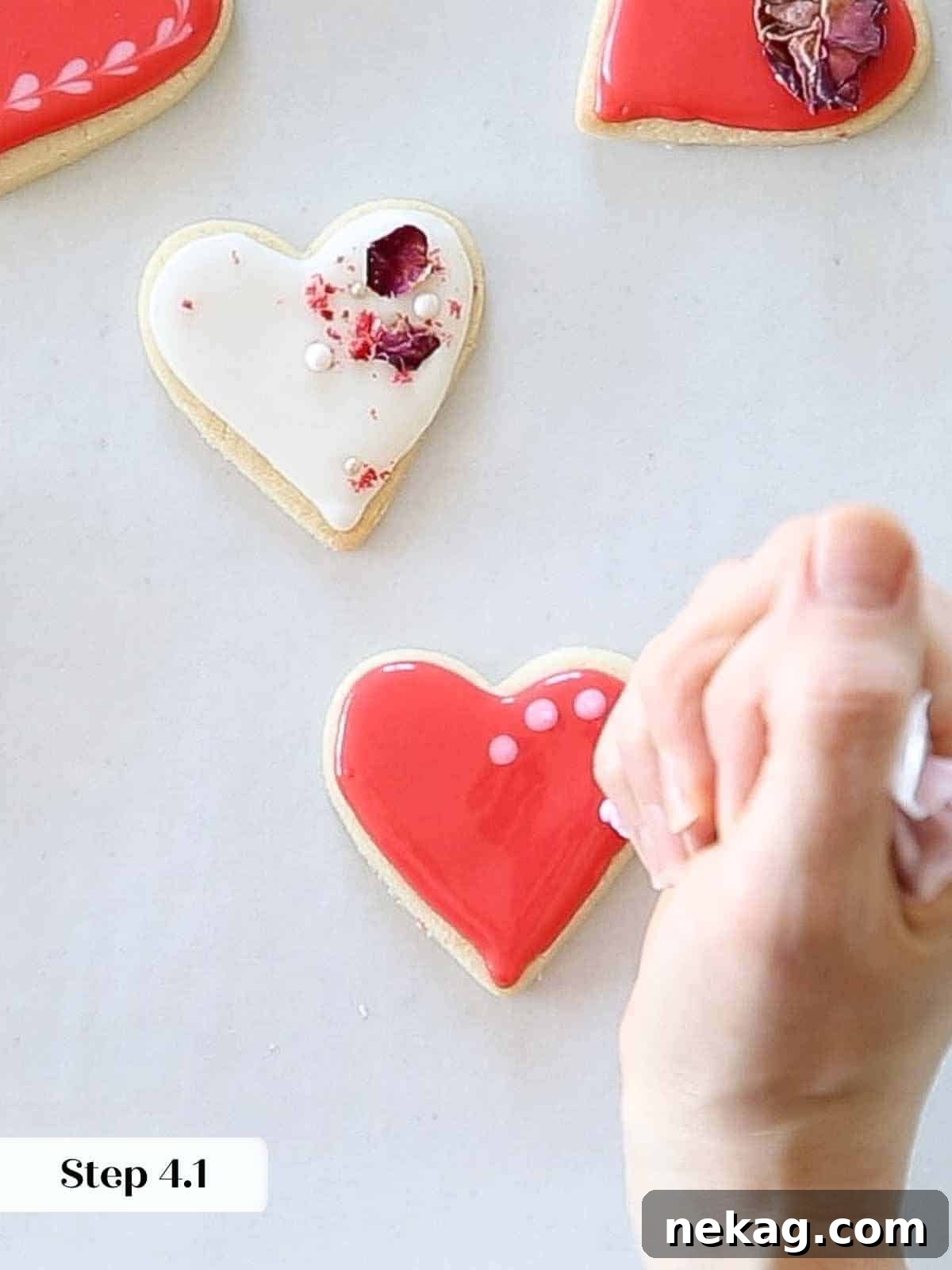 Sweetheart's Delight Cookies 14 Small dots of light pink royal icing piped onto a wet red flooded heart cookie, positioned for wet-on-wet heart technique.