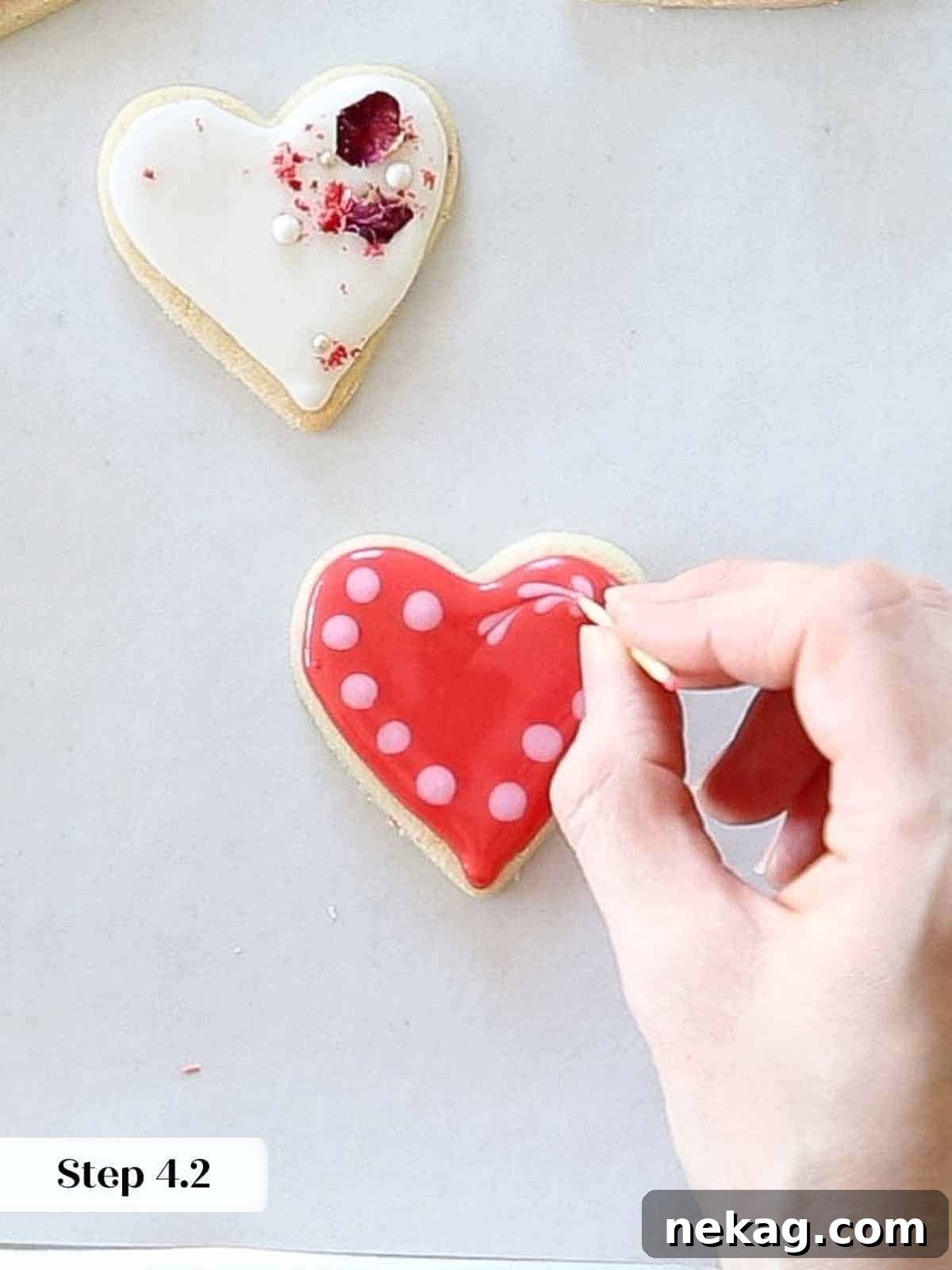 Sweetheart's Delight Cookies 15 A toothpick dragging through pink royal icing dots on a red flooded cookie to create small heart designs using the wet-on-wet technique.