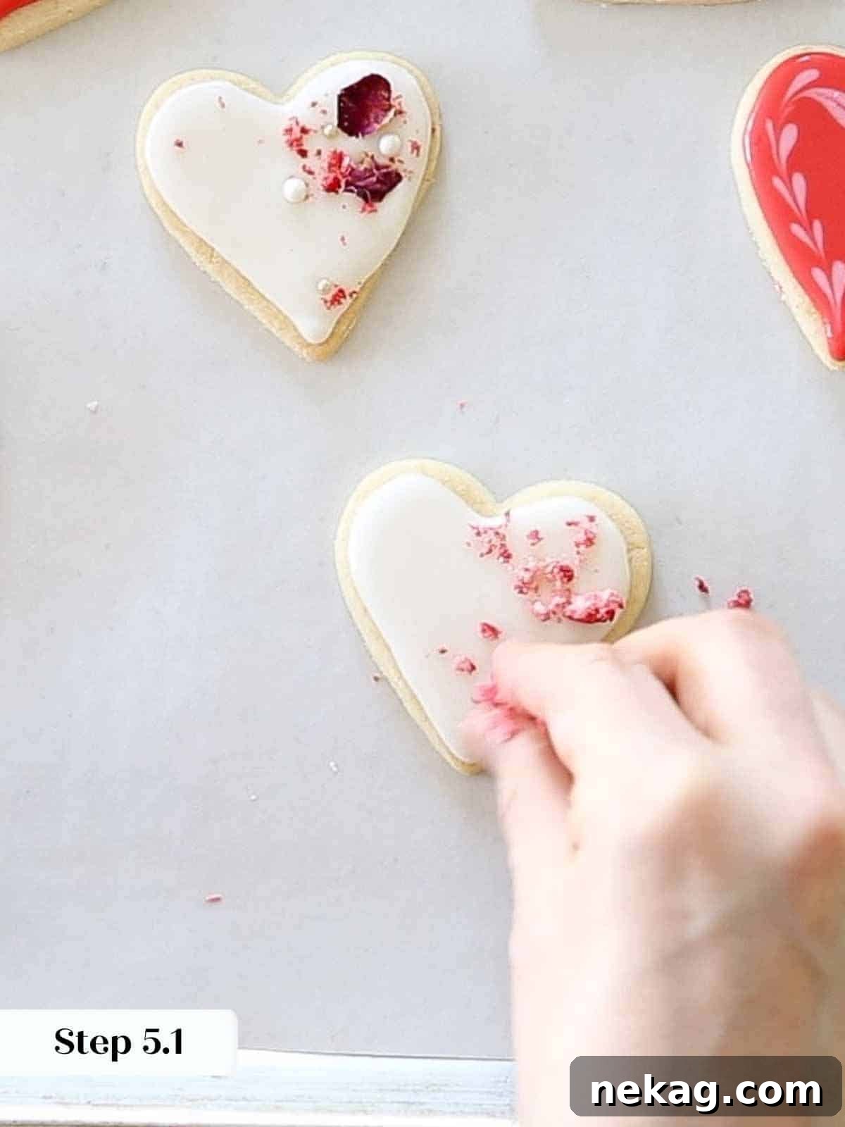 Rich Chocolate Sugar Cookies 11 Sprinkling dehydrated strawberry pieces onto white-iced heart cookies.