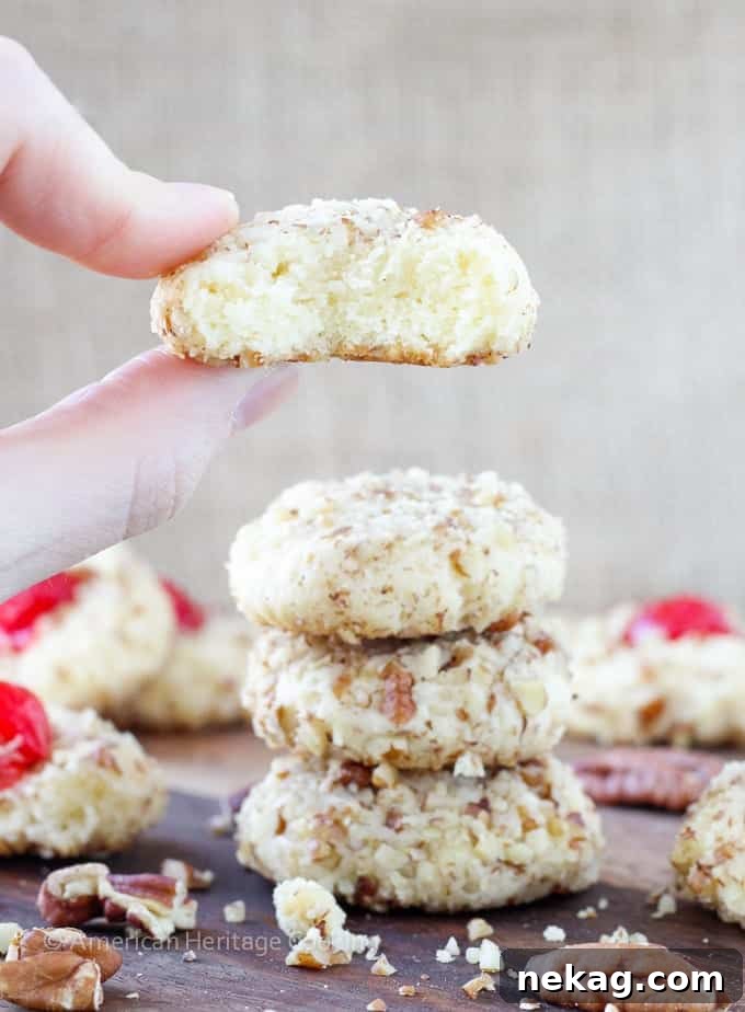 Close-up of freshly baked cherry pecan cookies, soft, chewy, nutty, with a cream cheese sugar cookie base and a vibrant maraschino cherry.