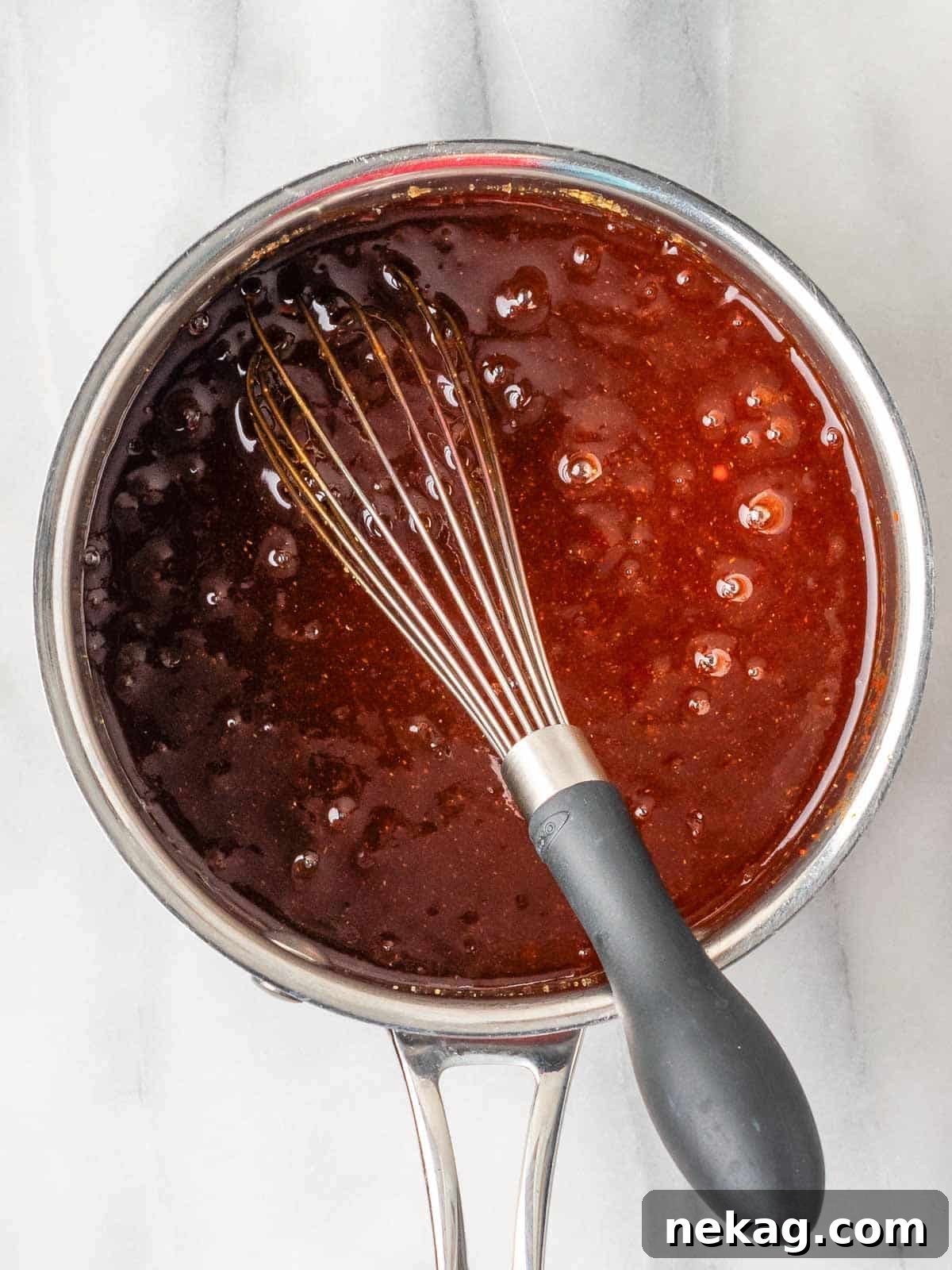 Homemade BBQ sauce simmering in a small pot with a whisk nearby, showcasing its rich texture and color.