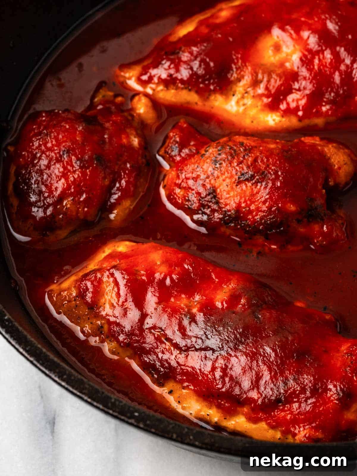 Perfectly cooked BBQ chicken in a cast iron skillet, coated generously with homemade sauce.