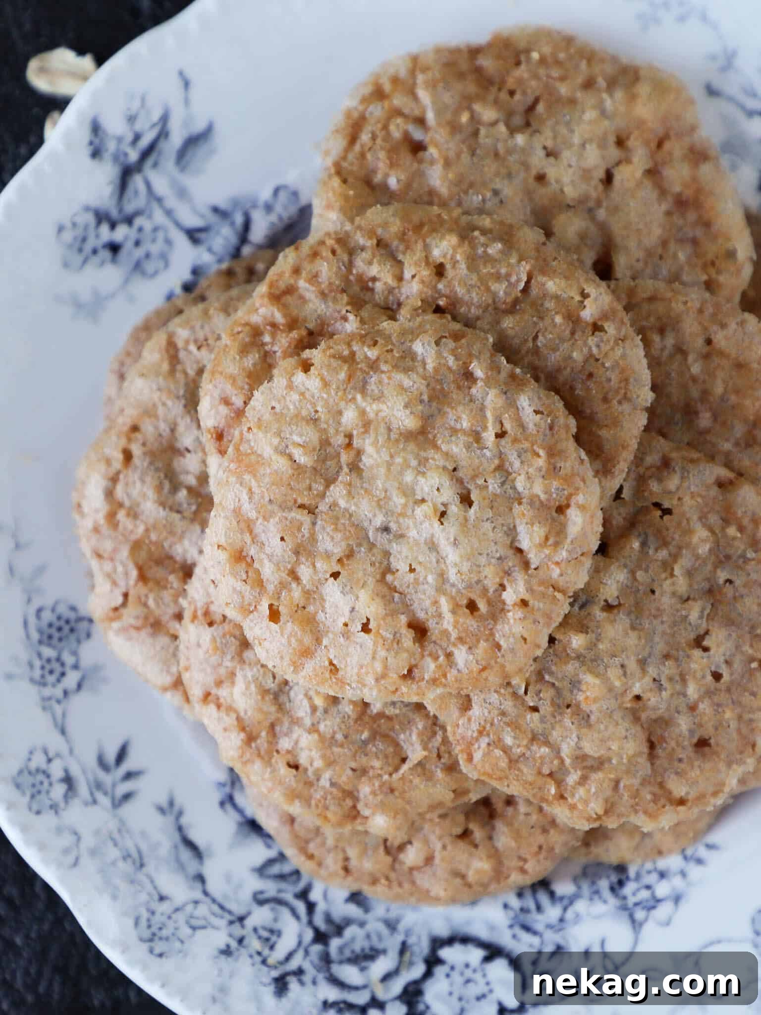 Golden brown oat lace cookies artfully arranged on a blue and white china plate, highlighting their delicate, lacy texture.