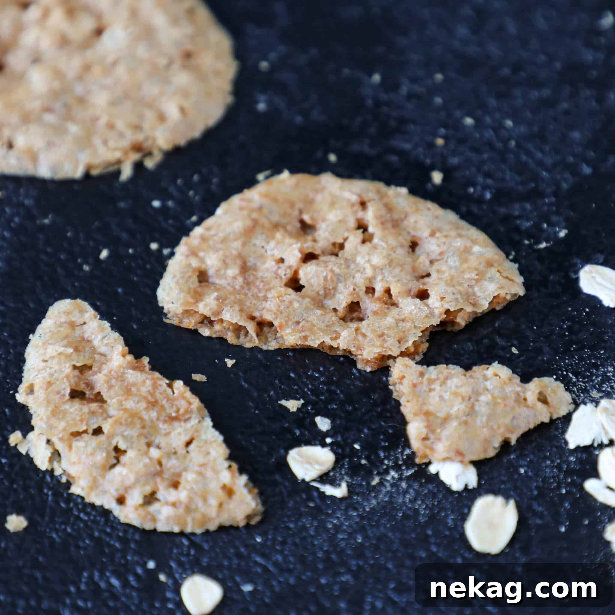 A delicate lace cookie, half-eaten, resting on a white surface, with scattered crumbs, showing its fragile beauty and inviting texture.