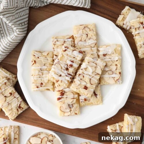 Thin rectangle almond bars with sliced almonds and drizzled glaze on a plate.