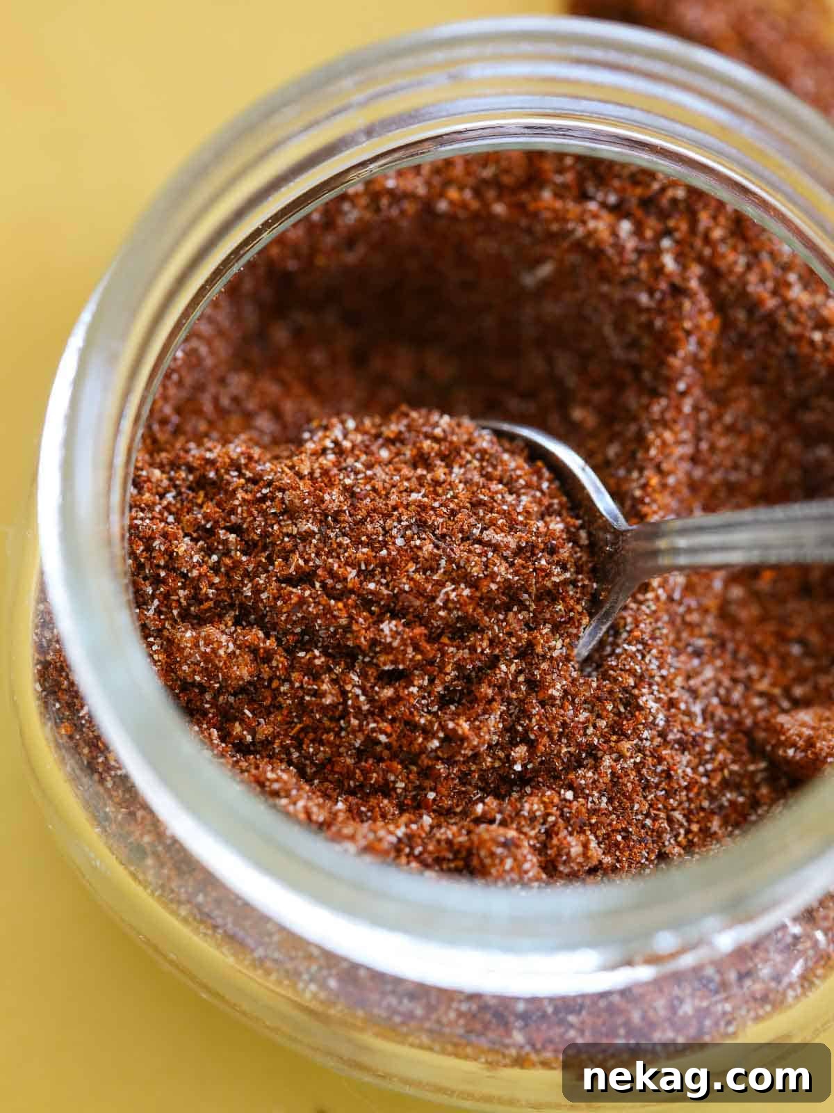 Homemade taco seasoning in a small glass jar, placed on a vibrant yellow plate, ready to be used.
