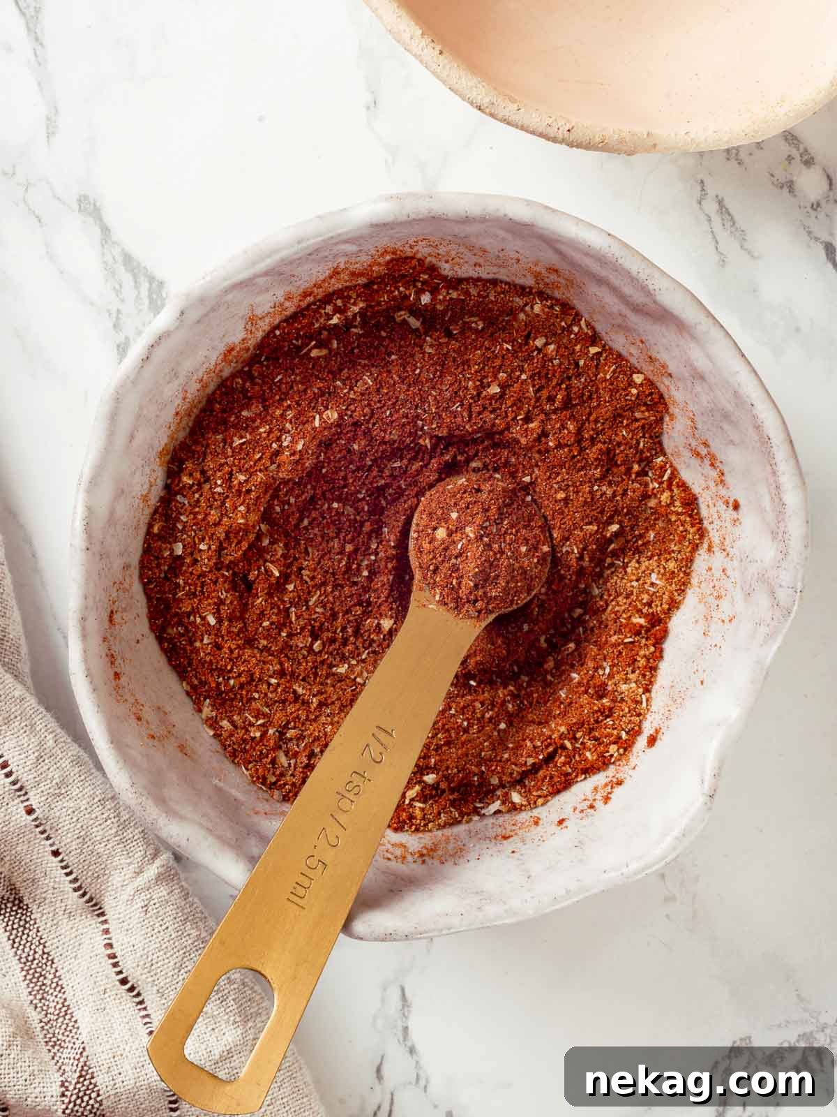 Homemade taco seasoning in a small white bowl, elegantly placed on a marble countertop.