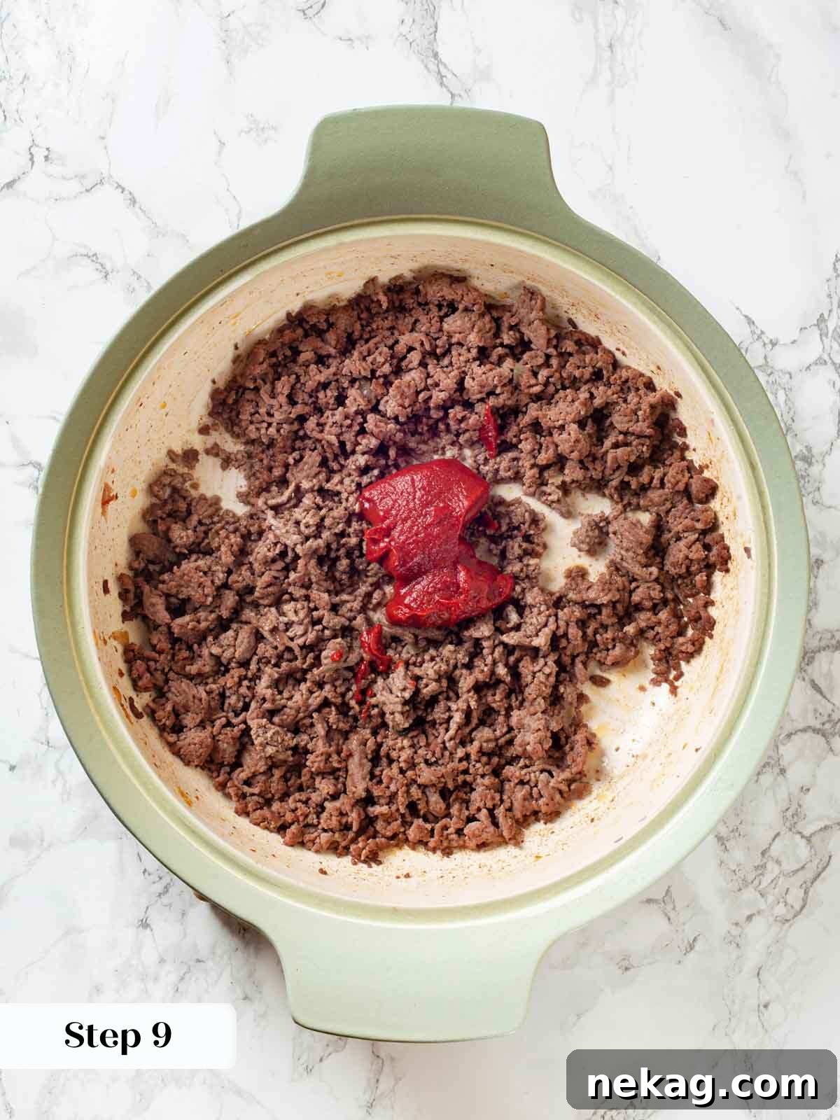 Adding tomato paste to cooked ground beef seasoned with spices in a skillet.