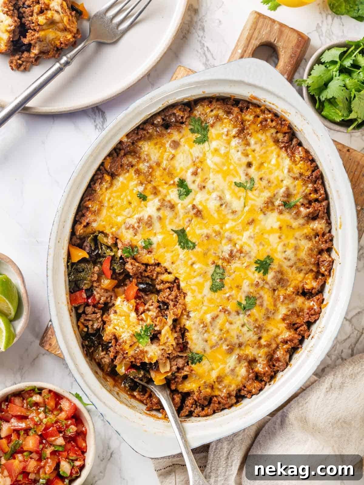 A white serving dish filled with the ready-to-eat taco bake, with a silver spoon poised to serve.