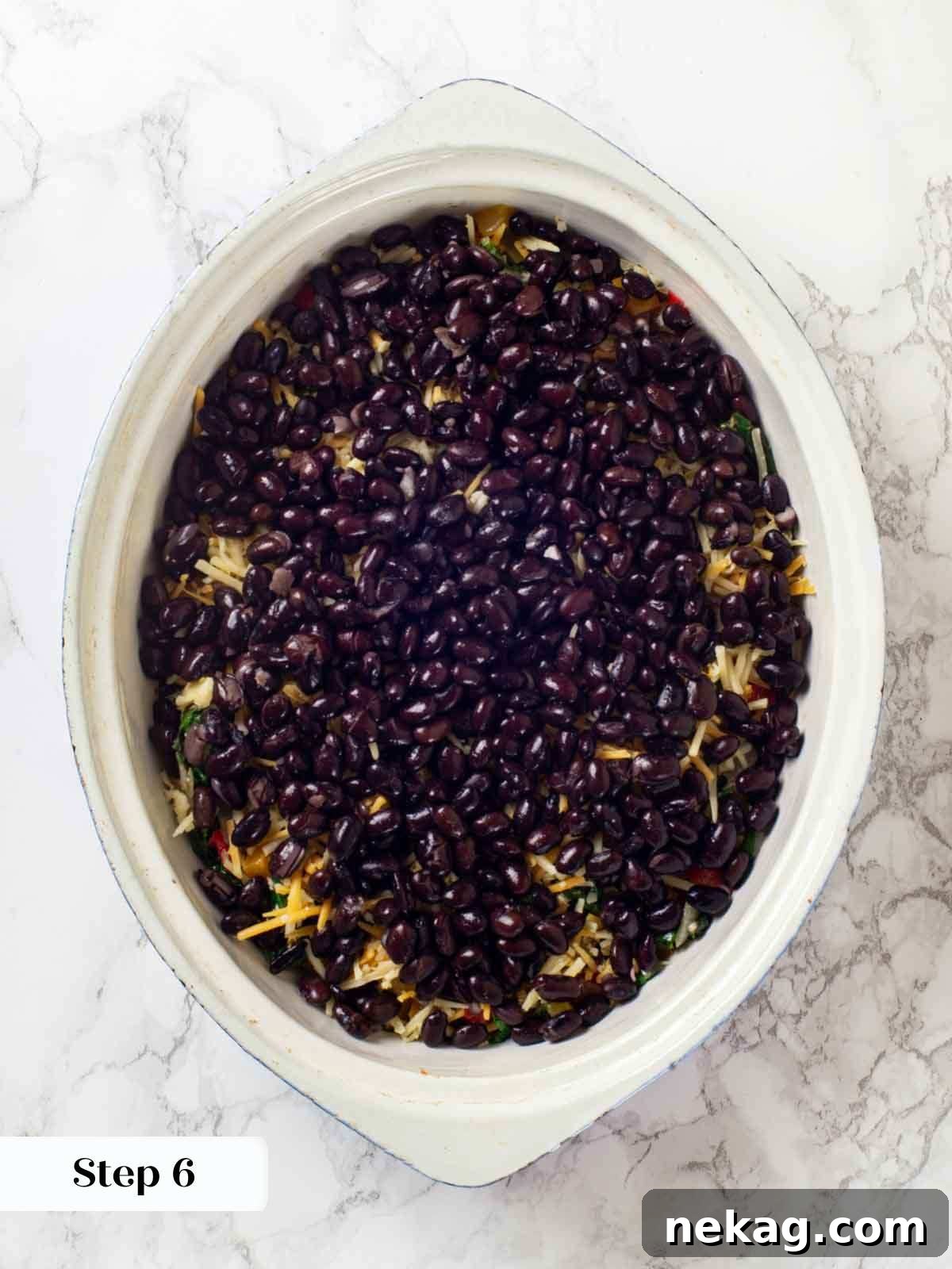 Black beans being added evenly over the vegetable layer in the taco casserole dish.