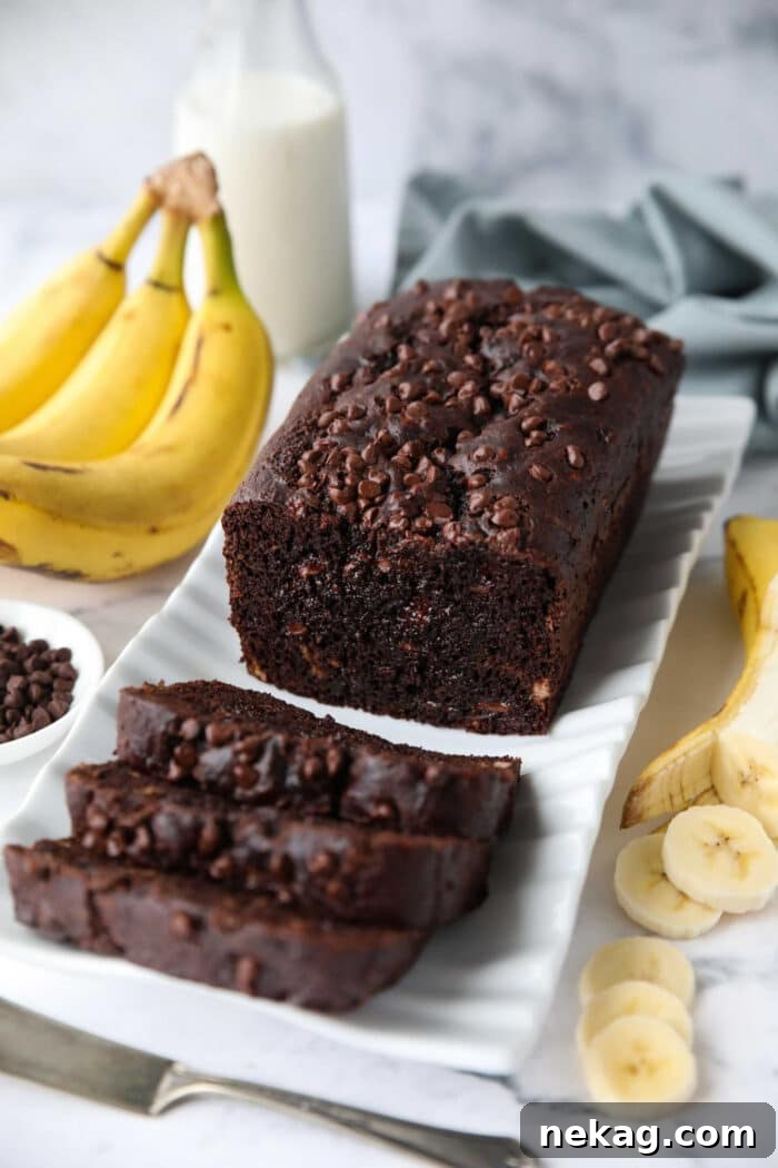 A beautifully presented chocolate banana bread on a serving plate, with several slices already cut, showing the soft, moist crumb and an abundance of chocolate chips.