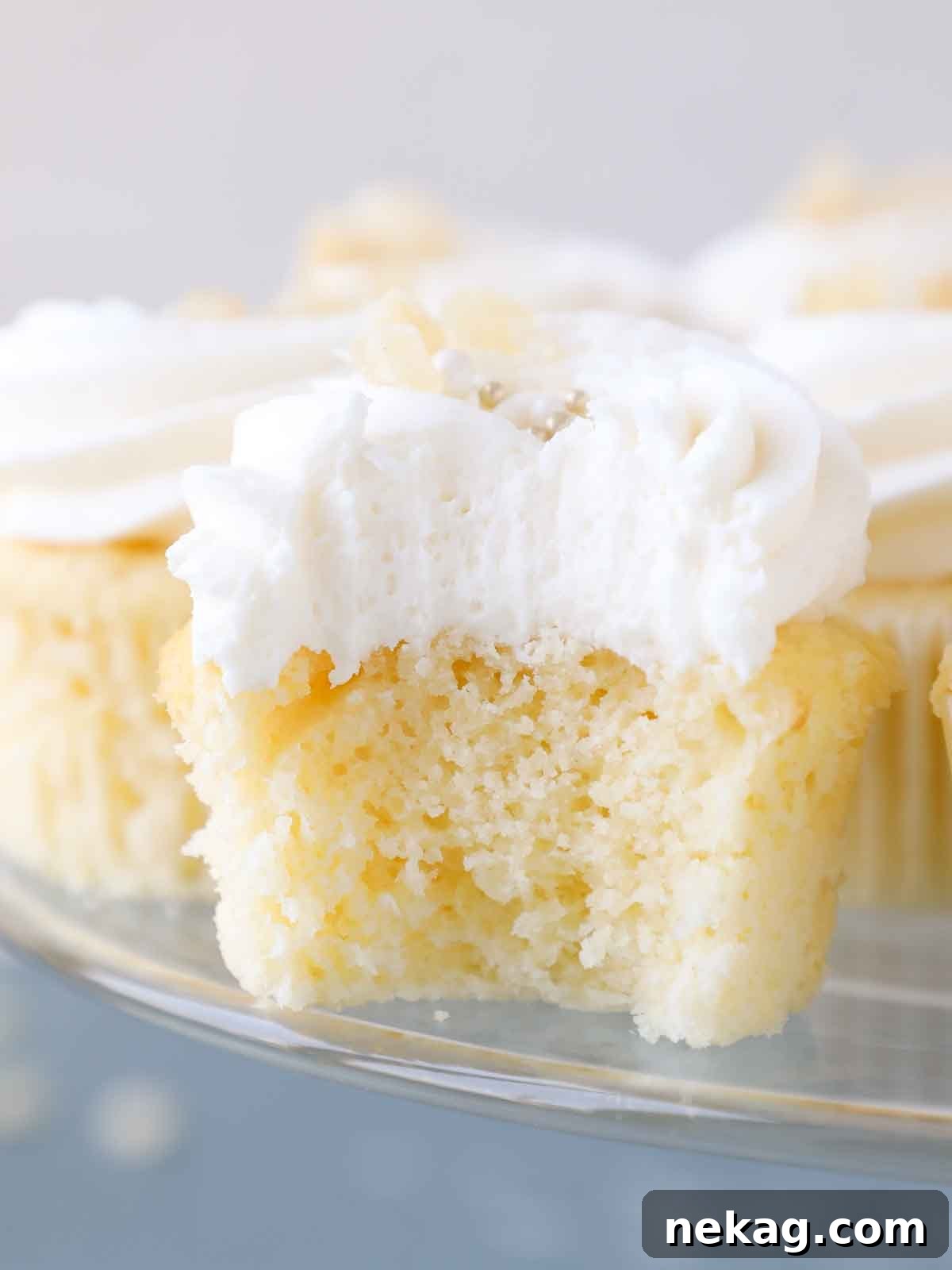 Sunshine Lemon Cupcakes 6 A close-up of the interior texture of a lemon cupcake, showing its light and fluffy crumb on a clear cake stand against a blue surface.