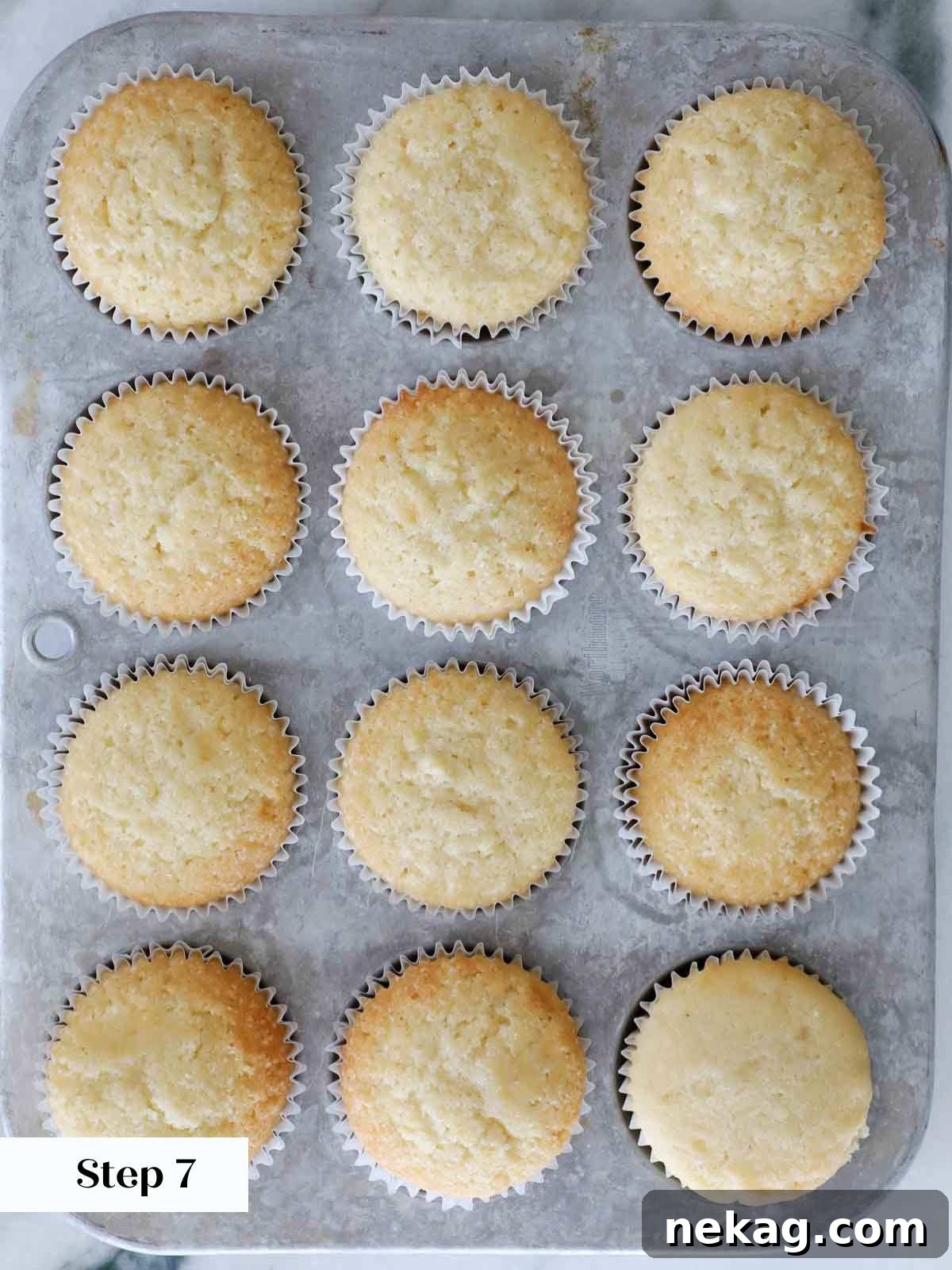 Fluffy Vanilla Delights 10 Baked vanilla cupcakes cooling in a metal tin.