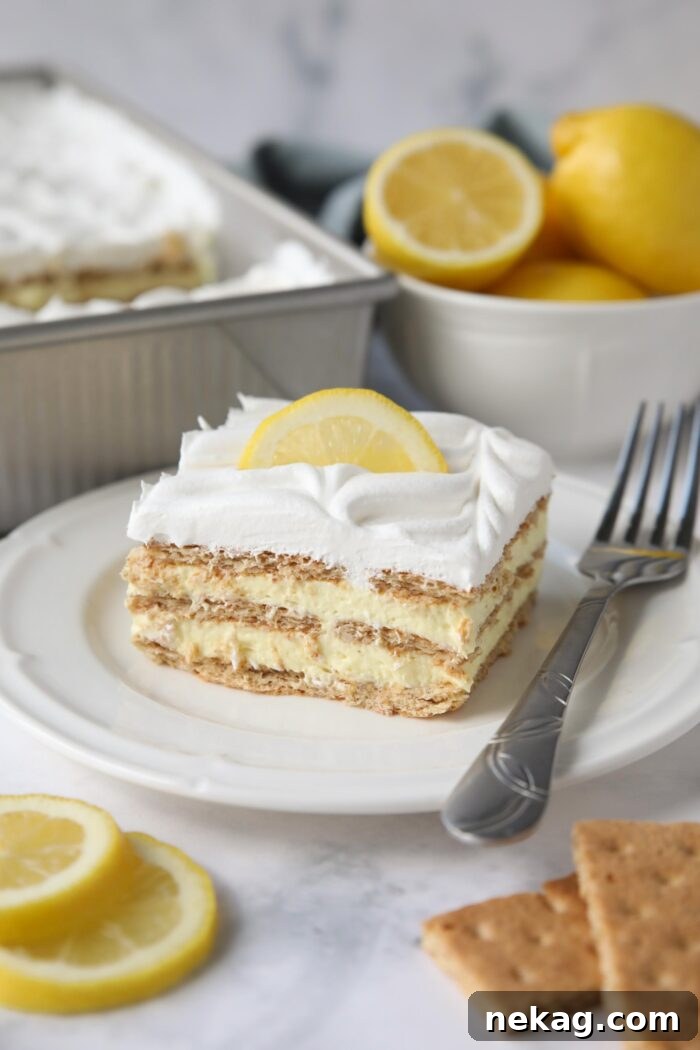 A perfectly sliced piece of lemon icebox cake, revealing its beautiful layers of golden graham crackers, pale yellow lemon pudding, and white whipped topping, on a white plate.