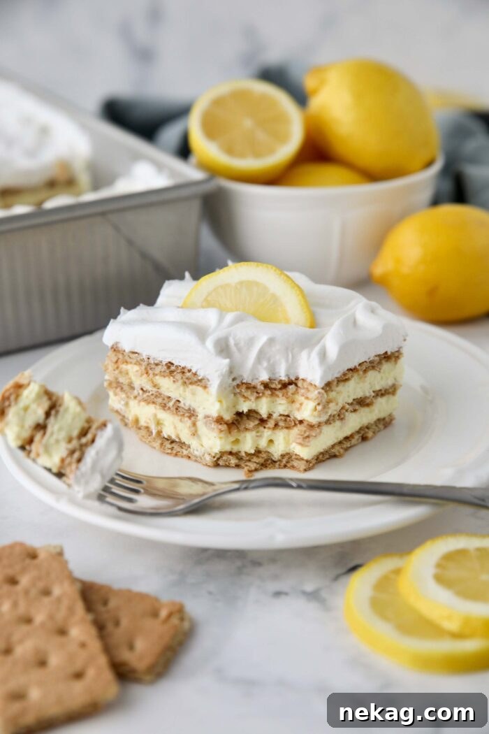 A fork taking a bite out of a slice of lemon icebox cake, showcasing the soft, cake-like graham cracker layers interspersed with creamy lemon pudding and fluffy whipped topping.
