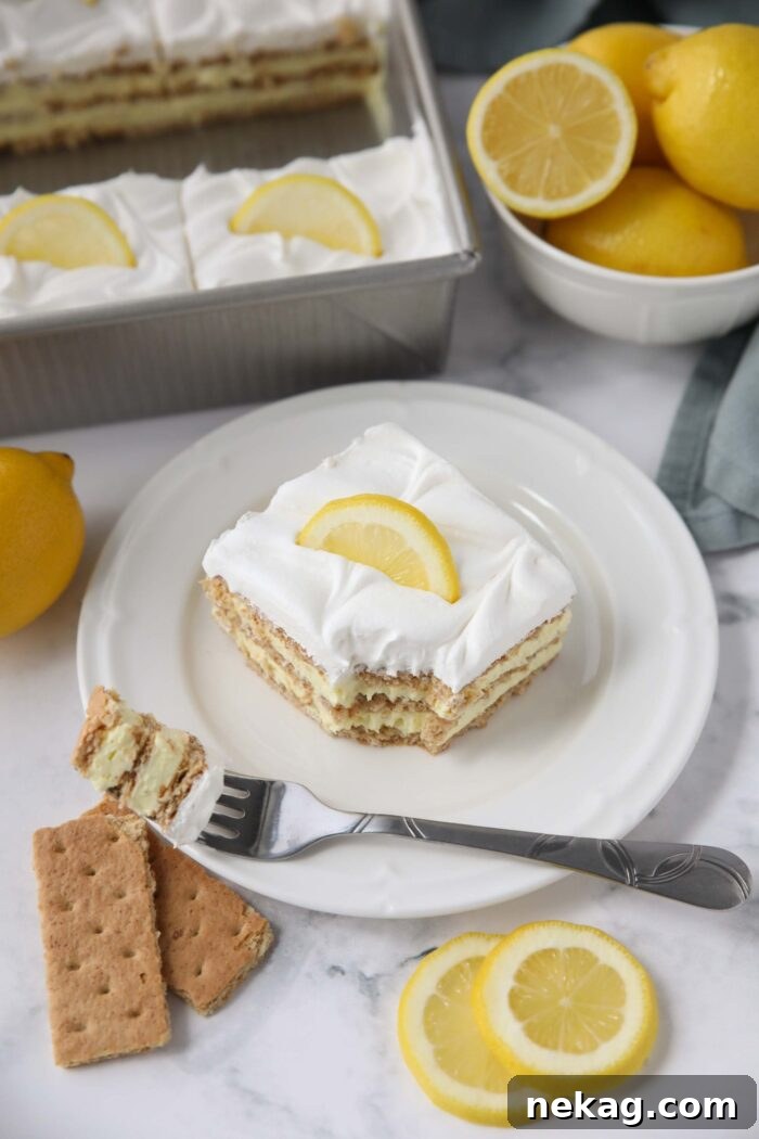 A fork taking a bite from a slice of lemon icebox cake, showing the soft layers of graham cracker, lemon pudding, and Cool Whip, ready to be enjoyed.