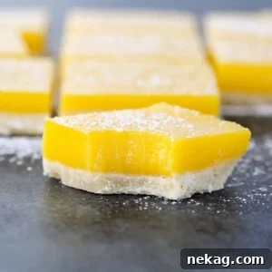 A close-up of an amazing lemon bar, showcasing the thick, vibrant lemon layer and crumbly shortbread crust.