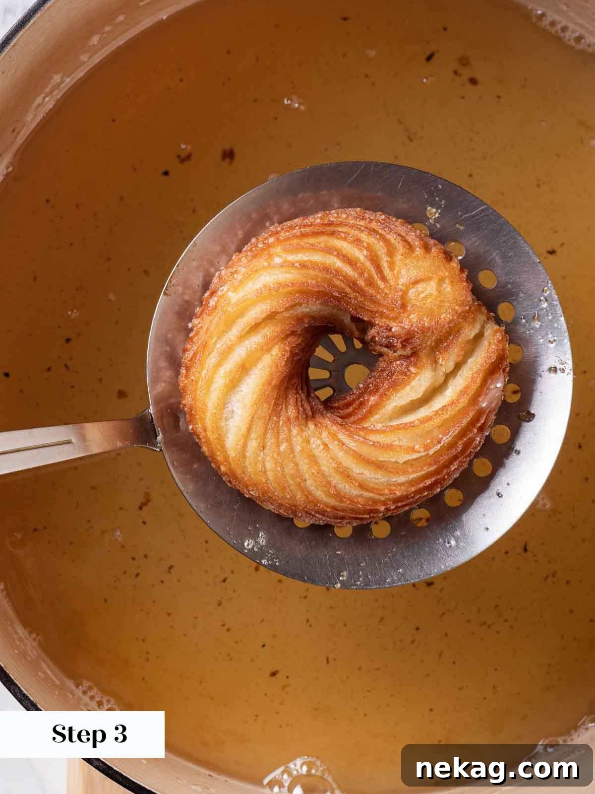 Rippled Golden Doughnuts 16 A perfectly fried French cruller being carefully lifted from the hot oil with a perforated spoon, showing its golden color and crisp texture.