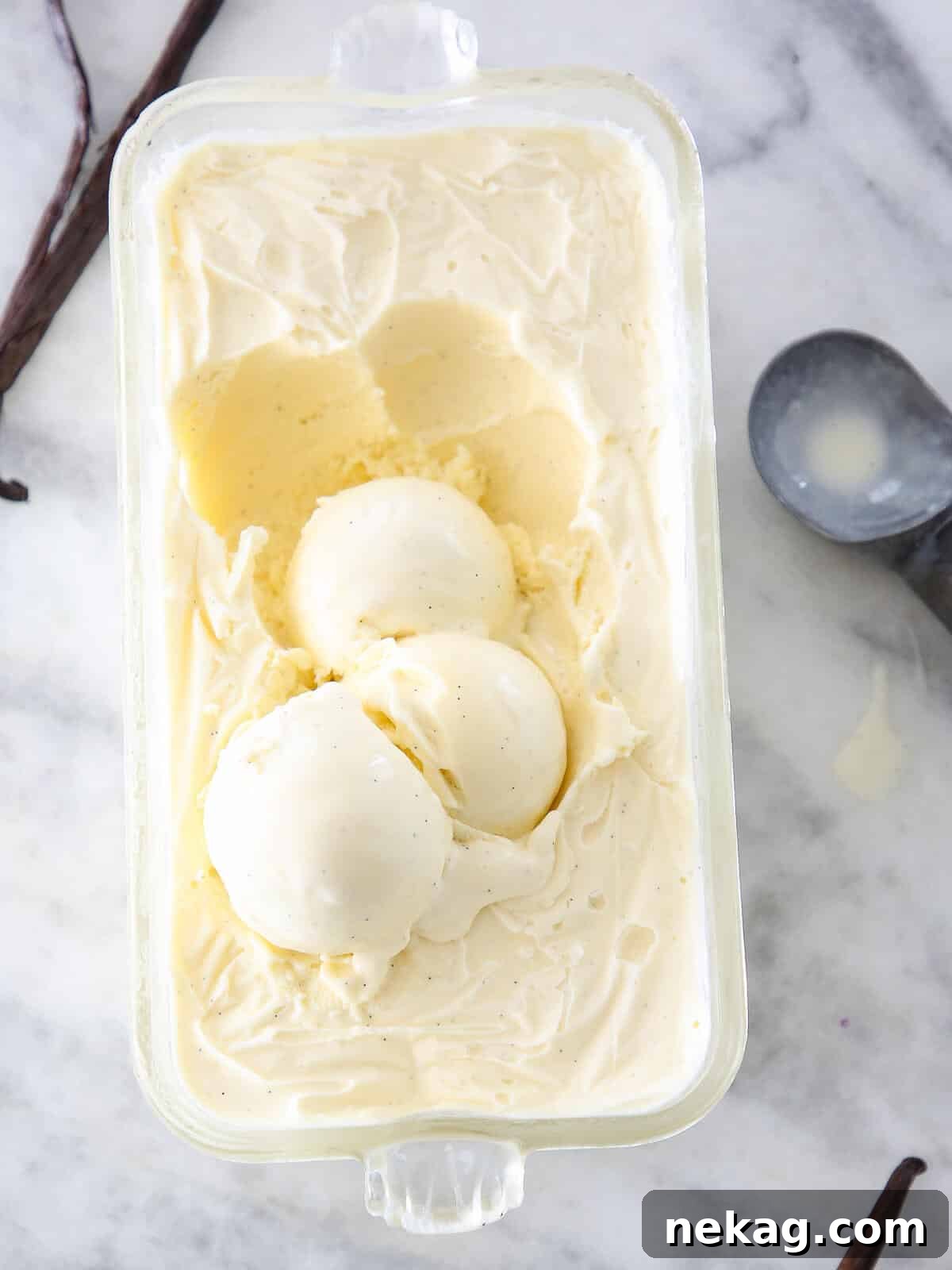 Velvet Vanilla Bean Indulgence 4 Three generous scoops of vanilla bean ice cream in a clear glass container on a elegant marble surface.