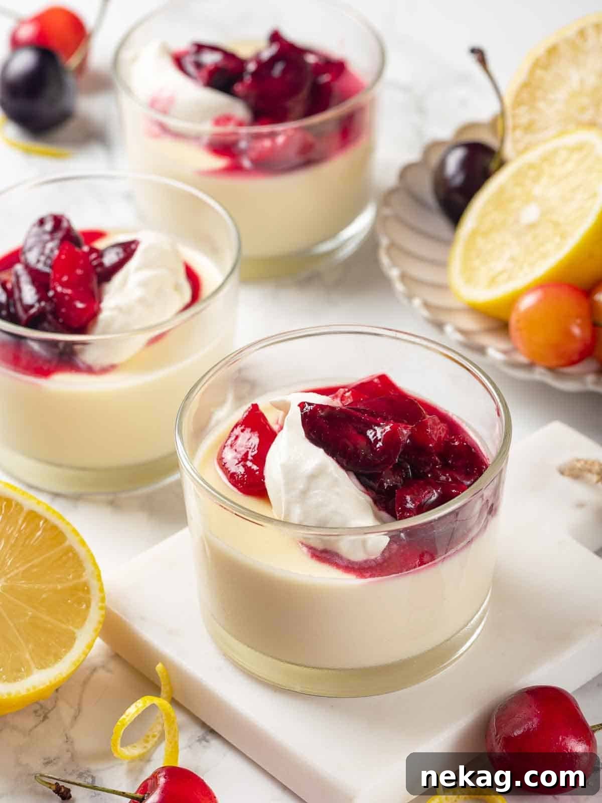 Velvet Lemon Delight 2 Three elegant glasses of lemon posset, beautifully garnished with homemade whipped cream and a luscious cherry sauce, ready to be served.