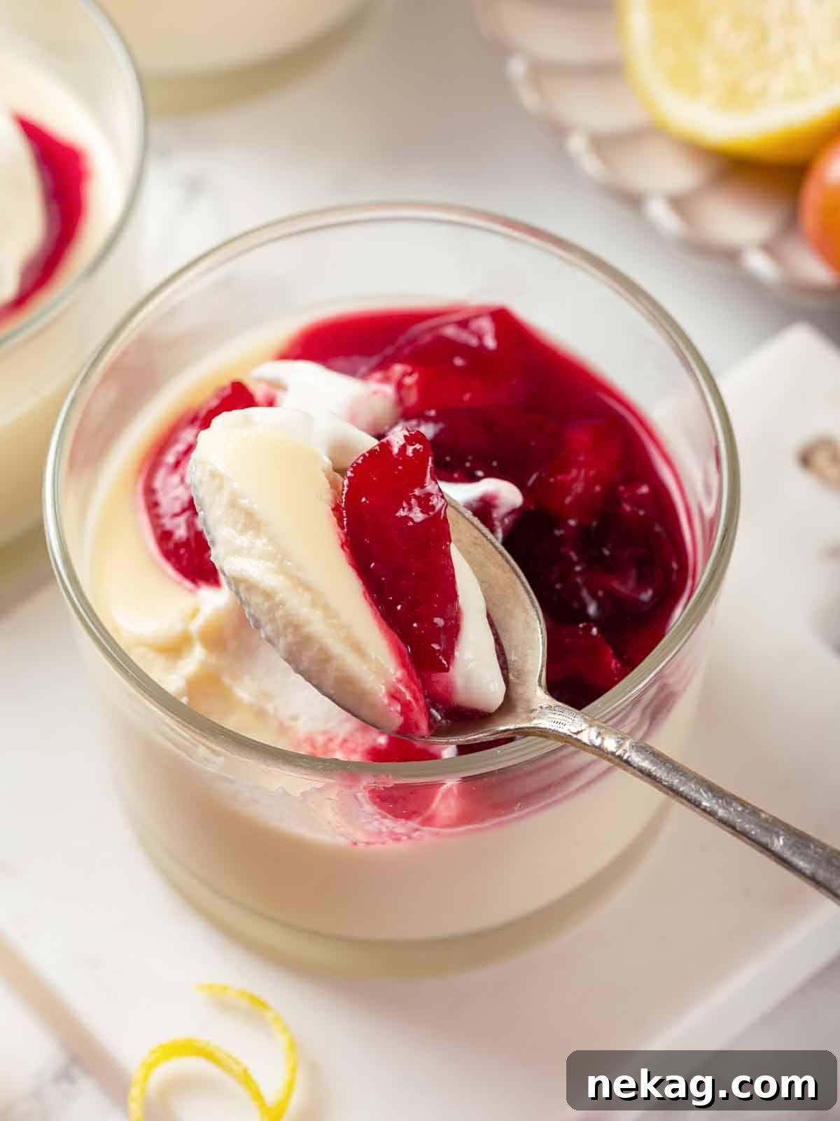 Velvet Lemon Delight 3 Close-up of a silver spoon taking a perfect bite of lemon posset, revealing its smooth, creamy texture, garnished with a glistening dollop of cherry sauce.