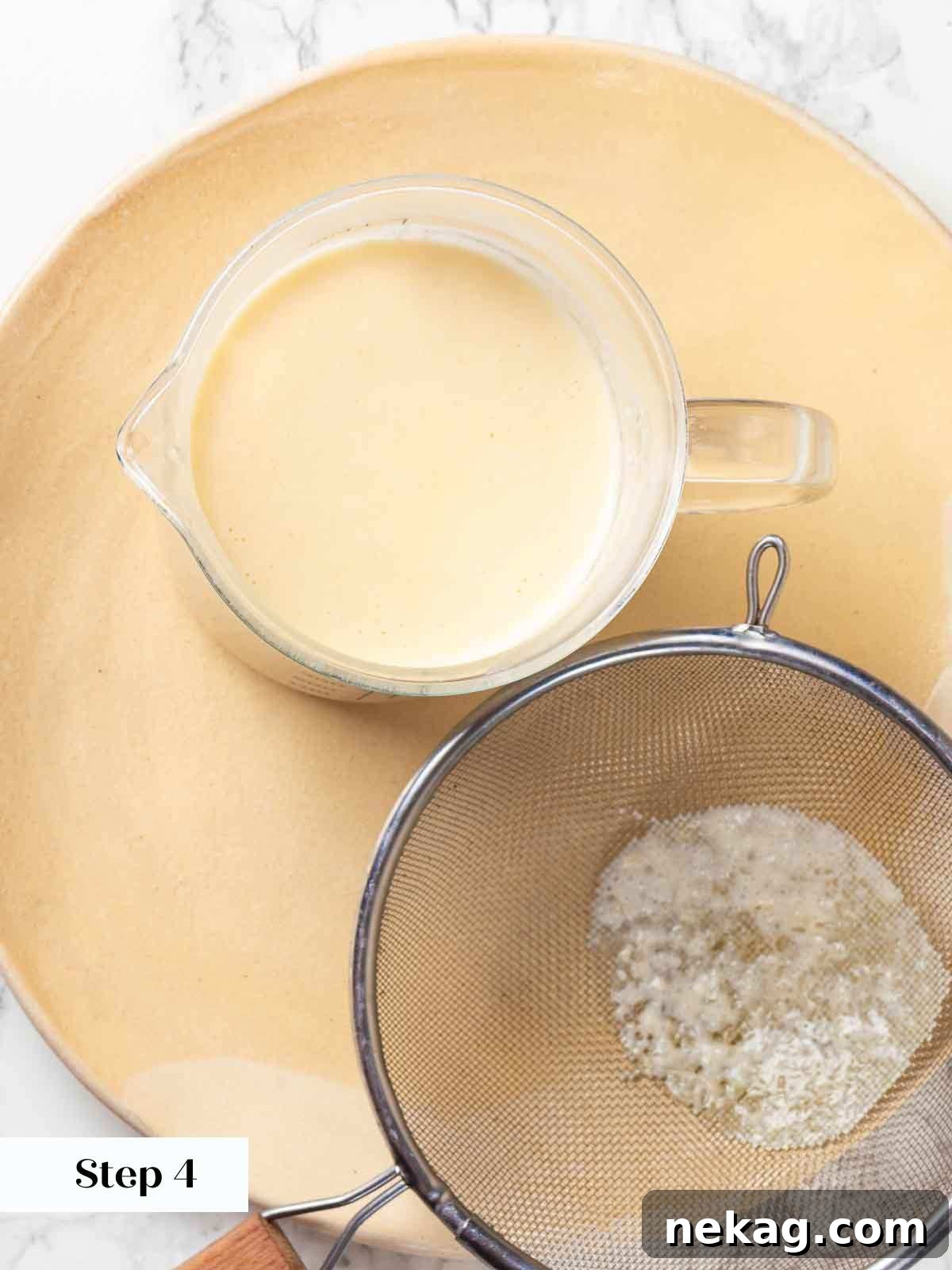 Velvet Lemon Delight 8 A fine-mesh sieve being used to strain the smooth lemon posset mixture into a clear glass measuring cup with a spout, ensuring a lump-free consistency.
