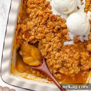 Warm Buttery Peach Crisp 14 A wooden serving spoon scooping a portion of peach crisp from a ceramic dish.