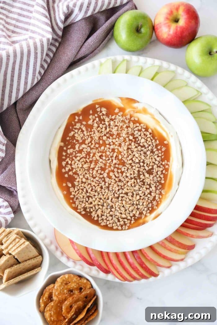 Overhead shot of a bowl of cream cheese caramel apple dip, generously topped with toffee bits, with fresh apple slices arranged neatly on the side, ready for dipping.