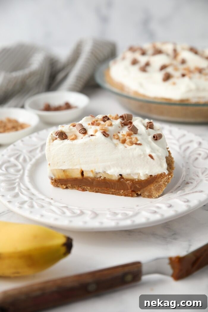 Effortless Banoffee Bliss 4 Side view of banoffee pie with graham cracker crust, dulce de leche, and whipped cream topped with toffee bits and chocolate shavings.