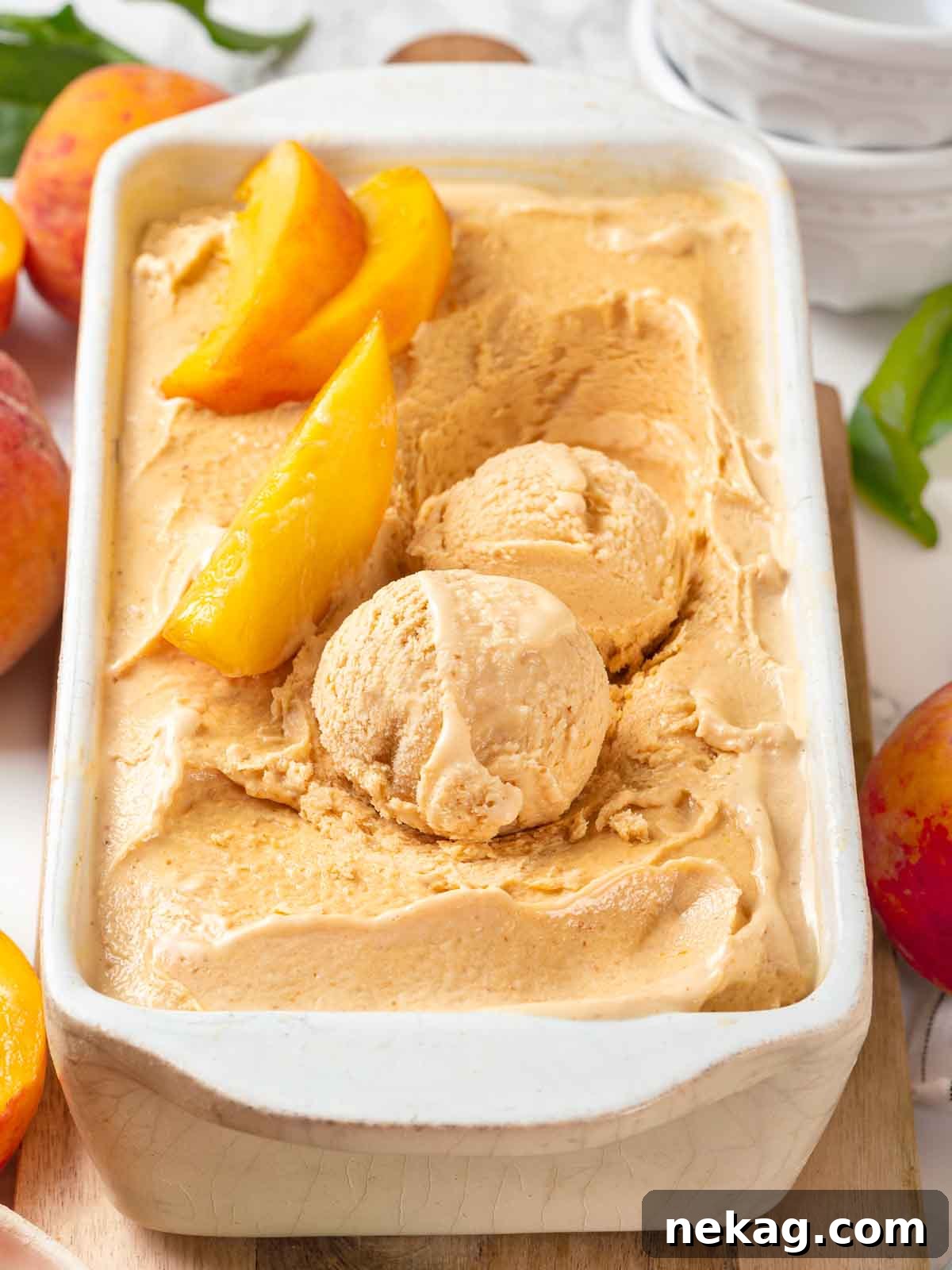 Fresh Peach Bliss 2 Scoops of vibrant, homemade peach ice cream in a white loaf pan, garnished with fresh peach slices, ready to be enjoyed.