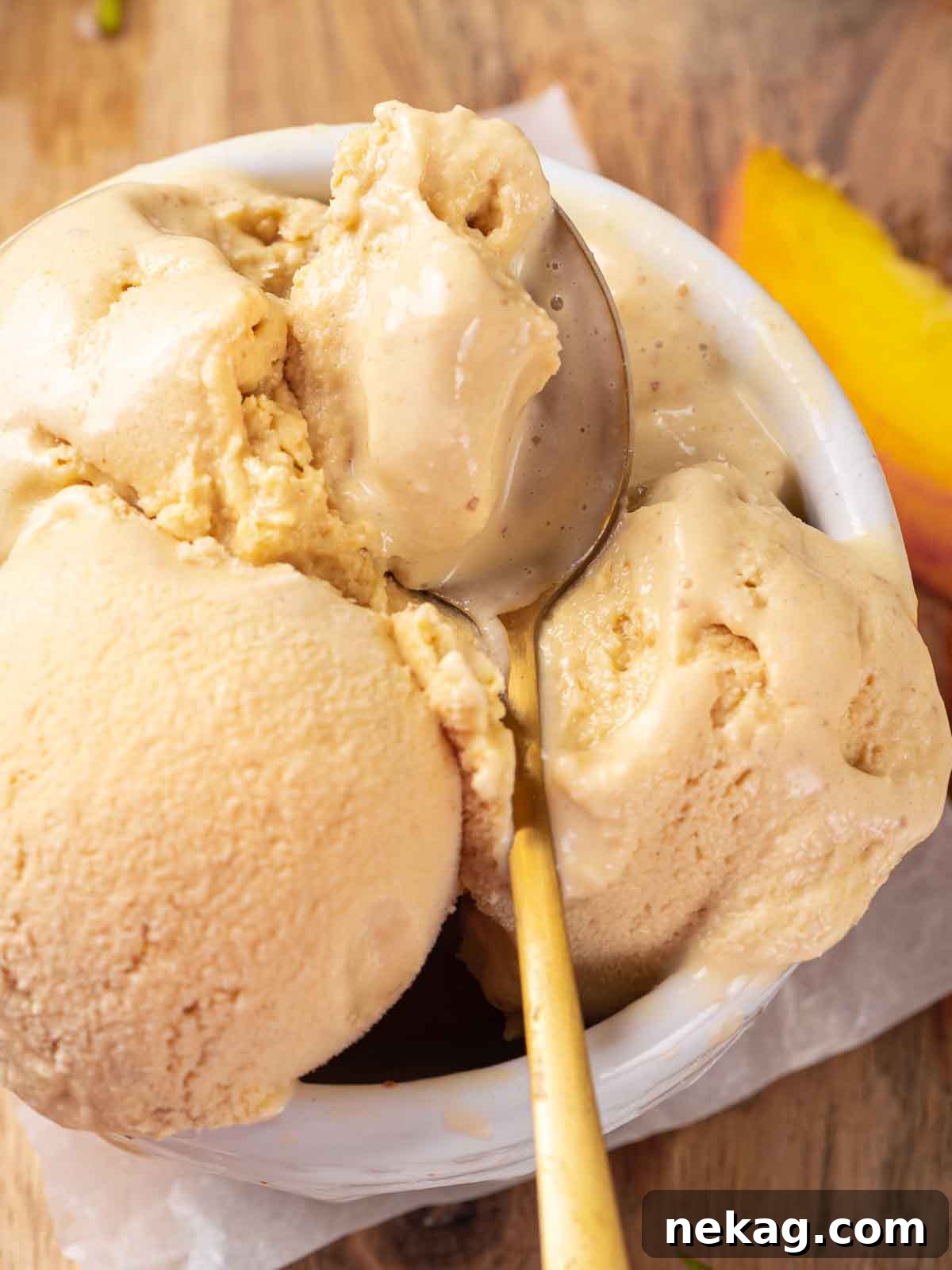 Fresh Peach Bliss 11 Close-up of two perfect scoops of homemade peach ice cream in a white bowl, elegantly served with a gold spoon.