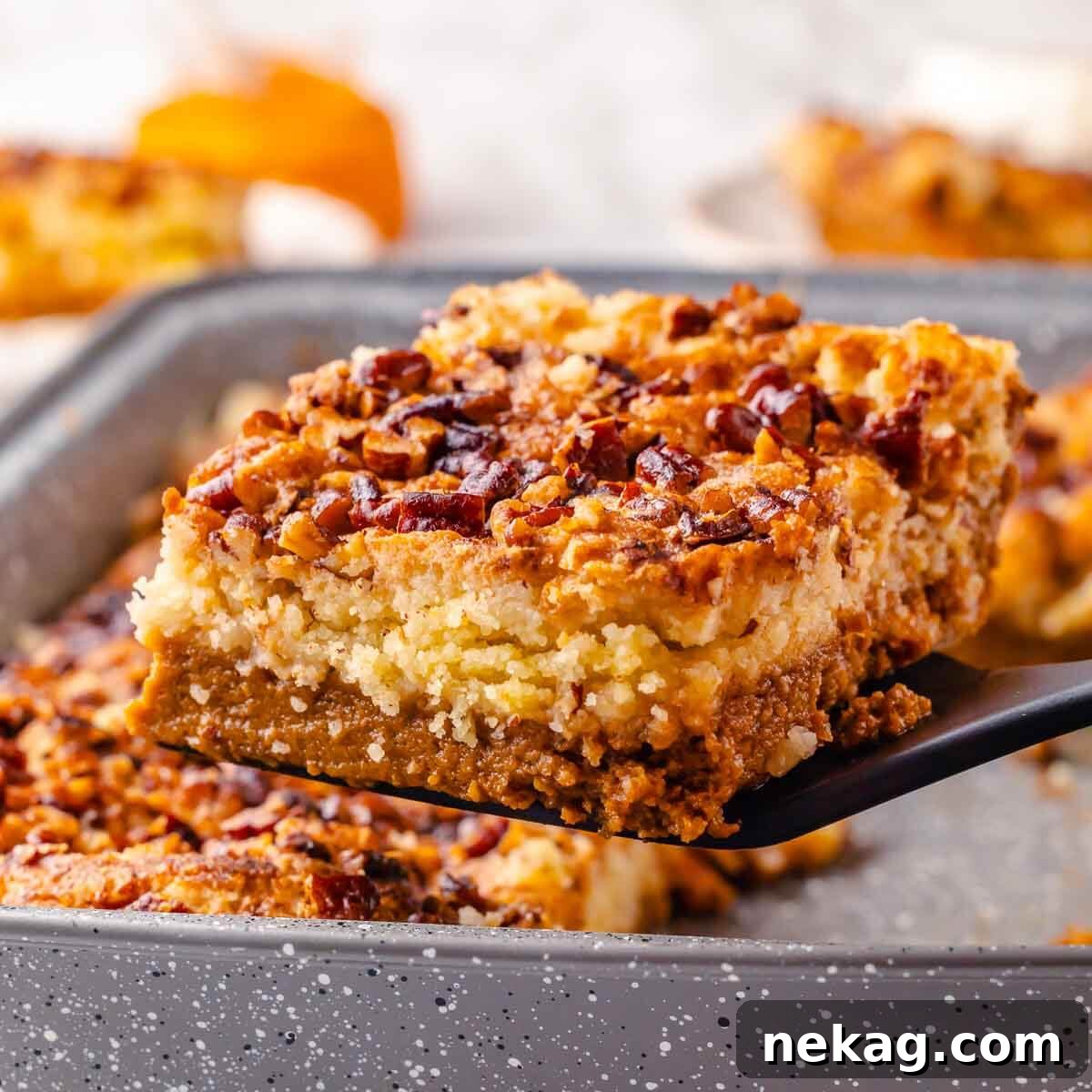 A server lifting a perfectly baked slice of pumpkin dump cake from the baking pan, showcasing its golden, crumbly crust and creamy, spiced pumpkin layers.