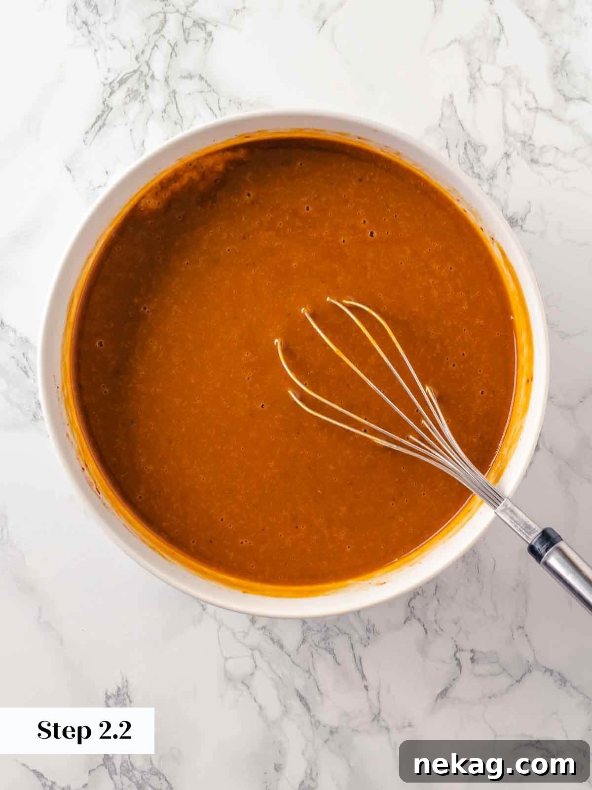 A large mixing bowl containing the perfectly whisked pumpkin dump cake ingredients, showcasing a smooth, uniform orange mixture ready for the next layering step.