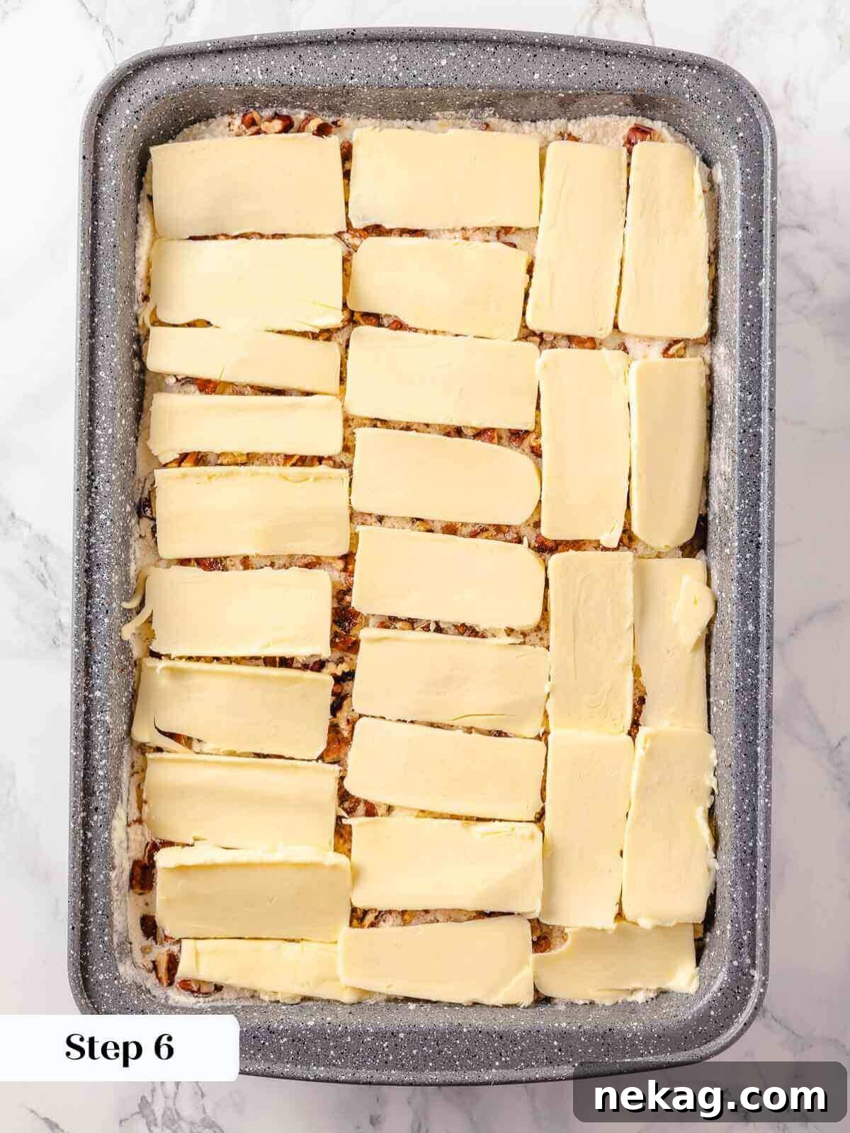 Thin, even slices of cold unsalted butter being carefully arranged in a single layer over the pecan-covered cake mix, the final step before the pumpkin dump cake goes into the oven.