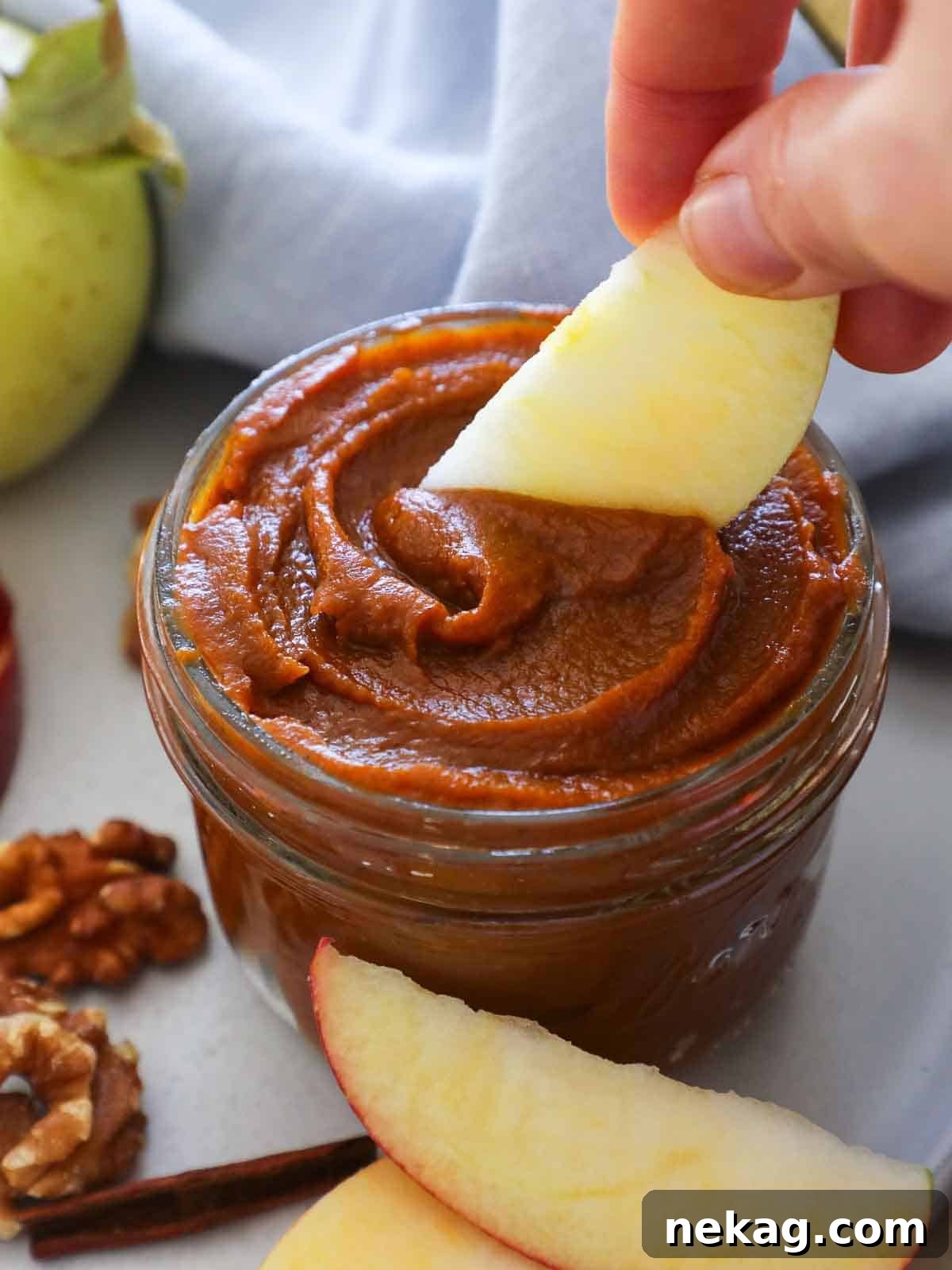 A jar of homemade pumpkin butter being scooped with a spoon, with a fresh apple slice in hand, suggesting a delightful pairing.