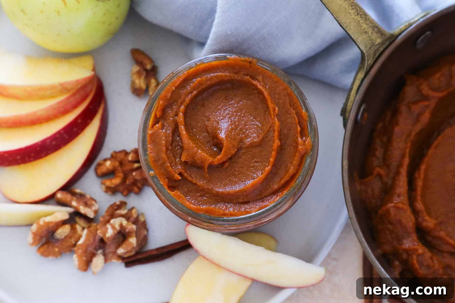 A charming fall arrangement featuring nuts, dried fruits, and a small jar of vibrant pumpkin butter, elegantly presented on a plate with a blue napkin, highlighting its aesthetic appeal.