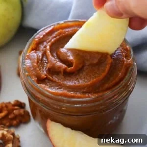 A spoonful of pumpkin butter being scooped from a jar, with a fresh apple slice beside it.