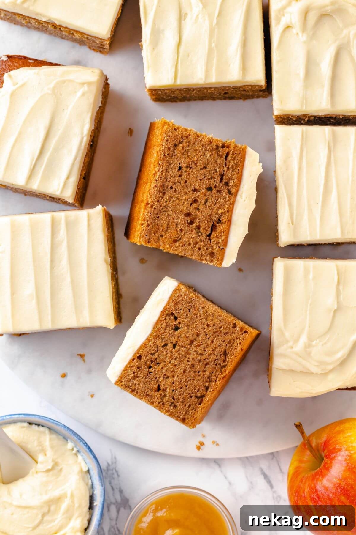 Spiced Applesauce Comfort Cake 21 Beautifully cut slices of applesauce cake, topped with creamy frosting, elegantly arranged on a marble surface.