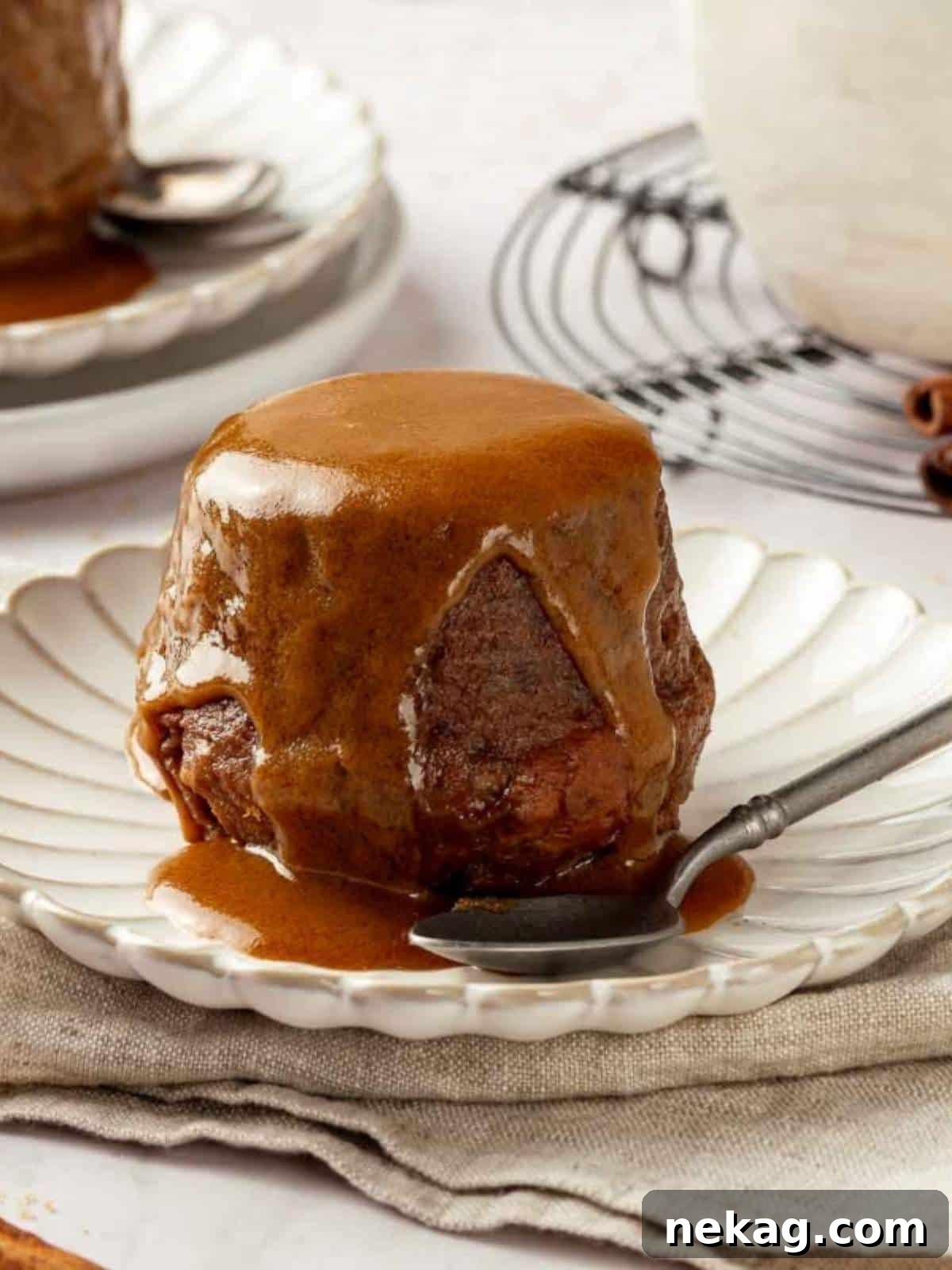 A single serving of sticky toffee pudding on a white plate, beautifully topped with a generous drizzle of toffee sauce.
