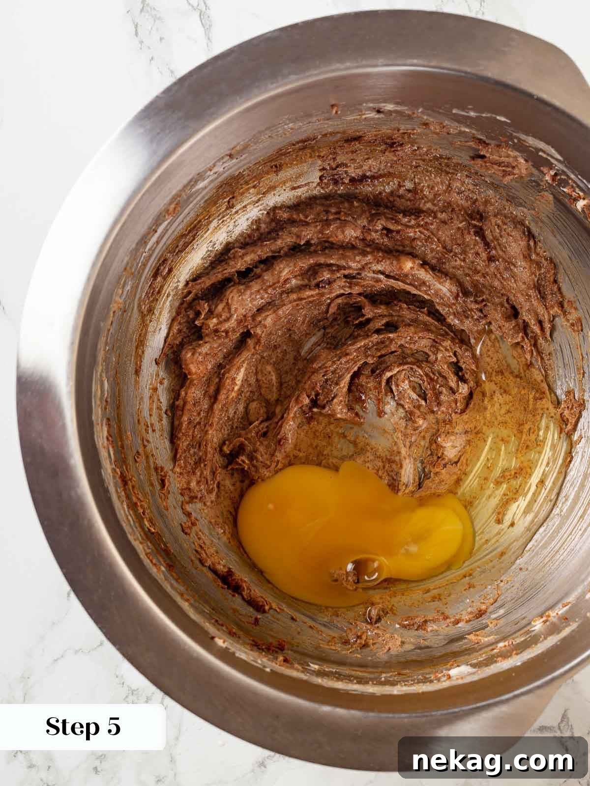 Eggs being added sequentially to the sticky toffee pudding batter in a mixing bowl for perfect emulsification.